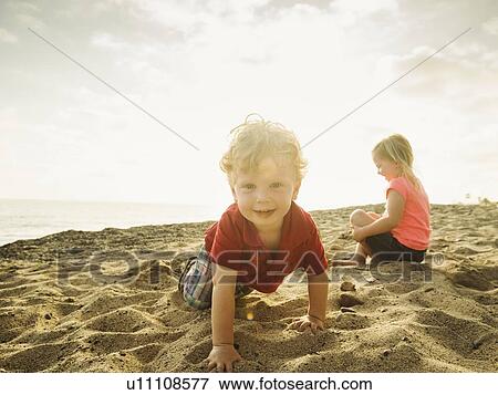 Stock Photo - Girl (4-5) and boy (2-3) playing on beach. Fotosearch