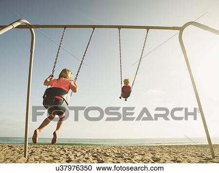 Girl (4-5) and boy (2-3) swinging on beach View Large Photo Image Stock Image - Girl (4-5) and boy (2-3) swinging on beach. Fotosearch