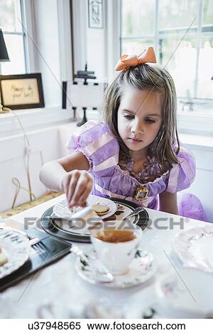 Stock Photography - Girl (4-5) eating cookies at dining table. Fotosearch