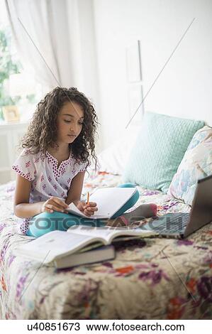 Stock Image - Girl (8-9) studying on bed. Fotosearch