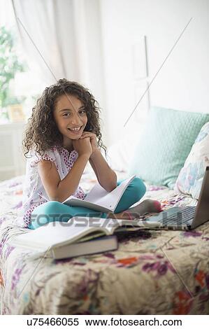 Stock Photography - Girl (8-9) studying on bed. Fotosearch