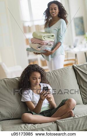 Girl (8-9) text messaging on sofa, mother in background View Large Photo Image Stock Photography - Girl (8-9) text messaging on sofa, mother in background. Fotosearch