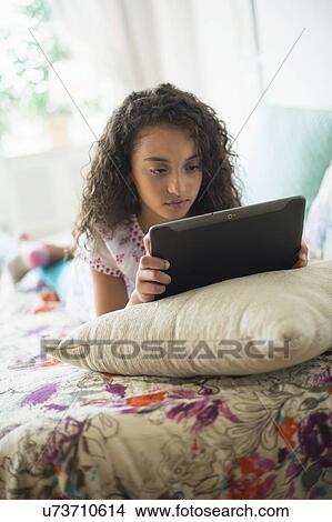 Picture - Girl (8-9) using digital tablet on bed. Fotosearch