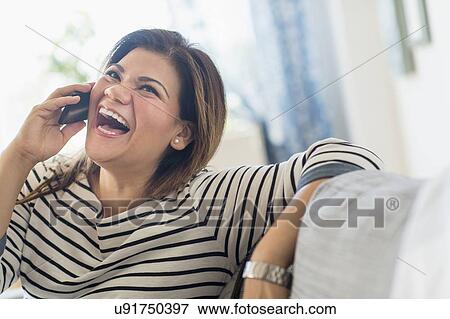 Happy woman sitting on sofa with mobile phone View Large Photo Image Stock Photo - Happy woman sitting on sofa with mobile phone. Fotosearch
