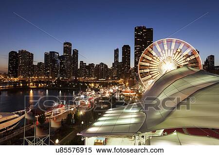 Stock Photography - Illuminated ferris wheel with skyscrapers in background. Fotosearch
