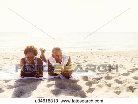 Stock Image - Man and woman reading on beach. Fotosearch