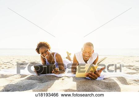 Stock Photograph - Man and woman reading on beach. Fotosearch
