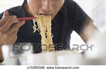 Stock Photo - Man eating noodles with chopsticks. Fotosearch