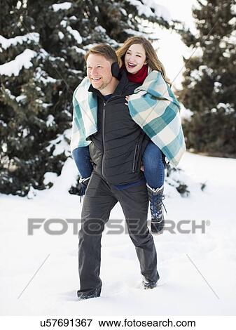 Stock Photo - Man giving woman piggyback ride in winter forest. Fotosearch