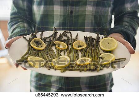 Stock Image - Man holding platter with asparagus and lemon. Fotosearch