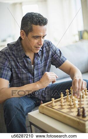 Stock Image - Man playing chess in living room. Fotosearch