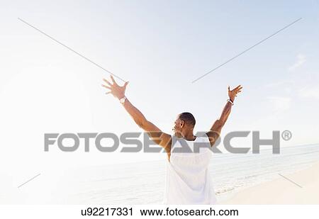 Stock Image - Man raising arms on beach. Fotosearch
