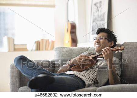 Man sitting on sofa and playing ukulele View Large Photo Image Stock Image - Man sitting on sofa and playing ukulele. Fotosearch
