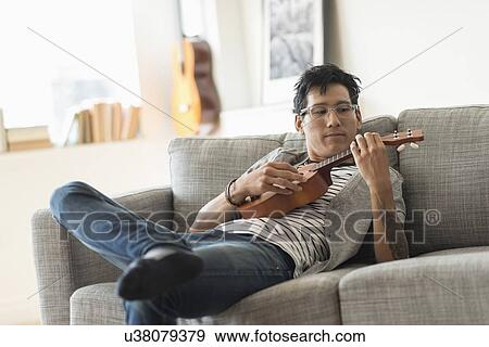 Man sitting on sofa and playing ukulele View Large Photo Image Stock Photo - Man sitting on sofa and playing ukulele. Fotosearch