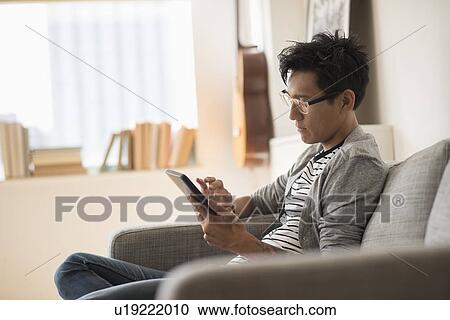 Man sitting on sofa and using tablet View Large Photo Image Stock Image - Man sitting on sofa and using tablet. Fotosearch
