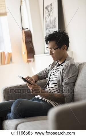 Man sitting on sofa and using tablet View Large Photo Image Stock Photography - Man sitting on sofa and using tablet. Fotosearch