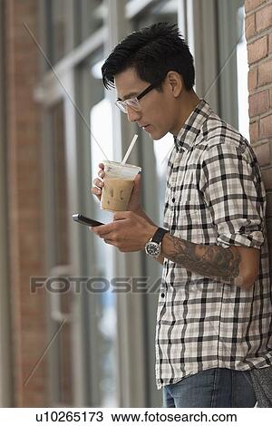 Stock Image - Man walking on sidewalk with iced coffee and mobile phone. Fotosearch