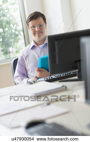 Picture - Man with down syndrome working in office. Fotosearch