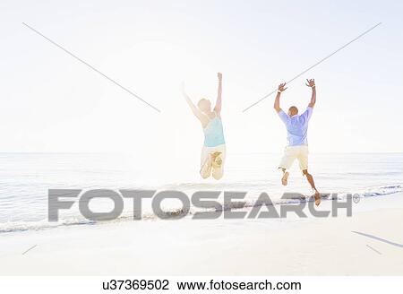 Mature couple jumping in sea with arms raised View Large Photo Image Stock Image - Mature couple jumping in sea with arms raised. Fotosearch