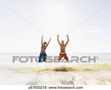 Stock Photo - Mature couple jumping in sea with arms raised. Fotosearch