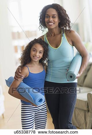 Stock Photo - Mother and daughter (8-9) holding yoga mats in living room. Fotosearch