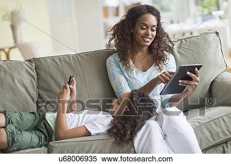 Stock Photography - Mother and daughter (8-9) relaxing on sofa. Fotosearch