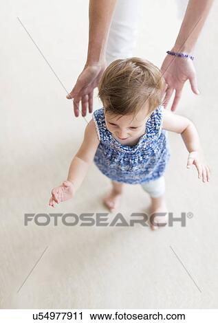 Stock Image - Mother assisting baby daughter (18-23 months) with her first steps. Fotosearch