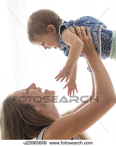 Stock Photograph - Mother lifting up baby daughter (18-23 months). Fotosearch