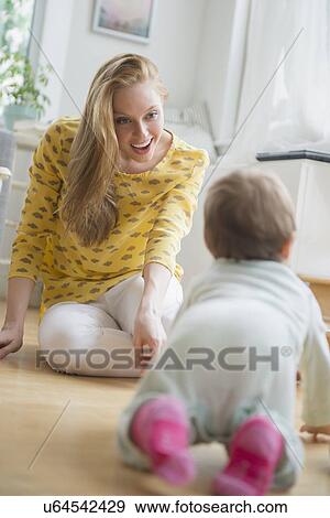 Stock Photo - Mother looking at baby daughter (6-11 months) crawling. Fotosearch