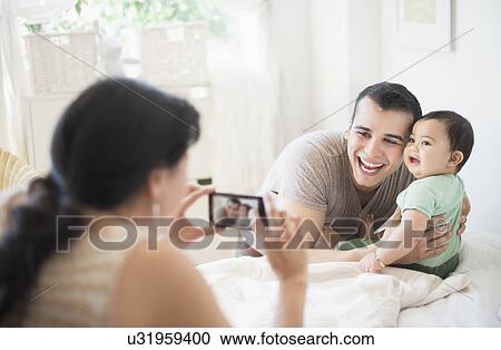 Mother photographing father with baby son (6-11 months) in bedroom View Large Photo Image Stock Image - Mother photographing father with baby son (6-11 months) in bedroom. Fotosearch