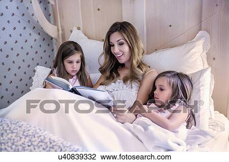 Stock Image - Mother reading bedtime story to her twin daughters (4-5). Fotosearch
