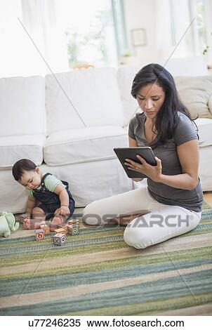 Mother using tablet pc while her son (6-11 months) playing with building blocks View Large Photo Image Stock Photography - Mother using tablet pc while her son (6-11 months) playing with building blocks. Fotosearch