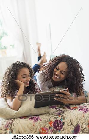 Mother with daughter (8-9) using digital tablet on bed View Large Photo Image Stock Photograph - Mother with daughter (8-9) using digital tablet on bed. Fotosearch