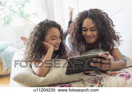 Mother with daughter (8-9) using digital tablet on bed View Large Photo Image Stock Photography - Mother with daughter (8-9) using digital tablet on bed. Fotosearch