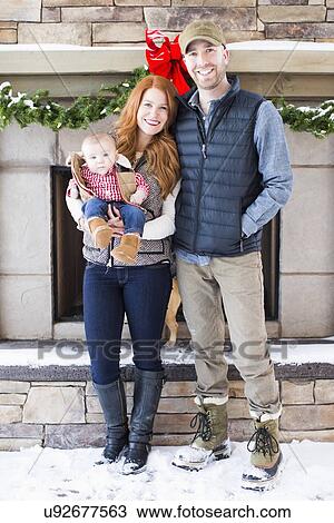 Stock Image - Portrait of family with one child (2-5 months) in front of house. Fotosearch