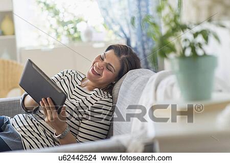 Picture - Portrait of happy woman lying on sofa with tablet pc. Fotosearch