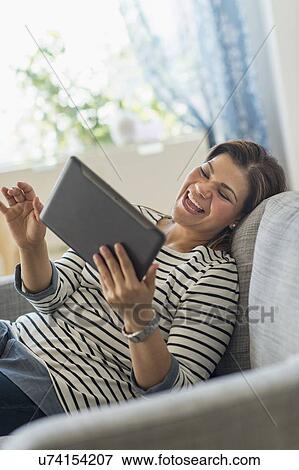 Portrait of happy woman lying on sofa with tablet pc View Large Photo Image Stock Photo - Portrait of happy woman lying on sofa with tablet pc. Fotosearch