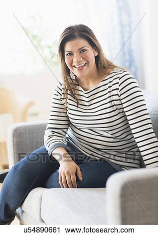 Stock Image - Portrait of happy woman sitting on sofa. Fotosearch