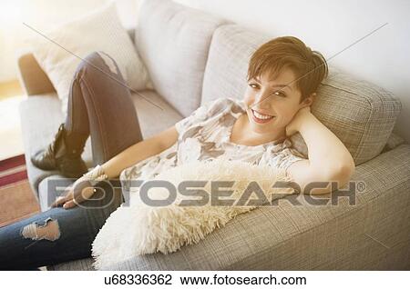 Stock Image - Portrait of smiling woman sitting on sofa. Fotosearch