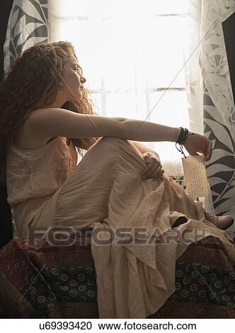 Stock Image - Portrait of stylish woman sitting in window sill. Fotosearch