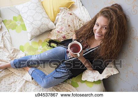 Stock Photo - Portrait of woman lying on bed with tea cup. Fotosearch