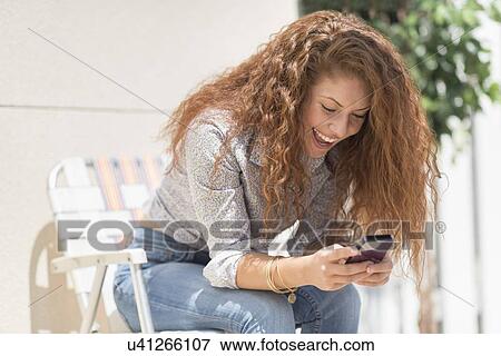 Portrait of woman sitting in deck chair outdoors with mobile phone View Large Photo Image Stock Photo - Portrait of woman sitting in deck chair outdoors with mobile phone. Fotosearch