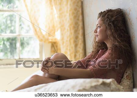 Stock Image - Portrait of woman sitting on bed. Fotosearch