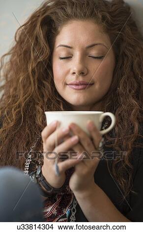 Picture - Portrait of woman sitting on bed with tea cup and closed eyes. Fotosearch