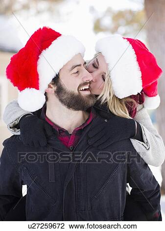 Stock Image - Portrait of young couple in santa hats, piggyback. Fotosearch