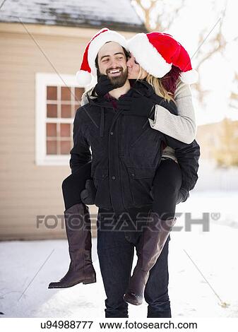 Stock Photo - Portrait of young couple in santa hats, piggyback. Fotosearch