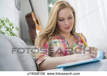 Portrait of young woman writing journal on sofa View Large Photo Image Stock Photograph - Portrait of young woman writing journal on sofa. Fotosearch