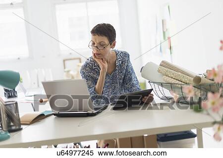 Stock Photography - Senior business woman using laptop and tablet in office. Fotosearch