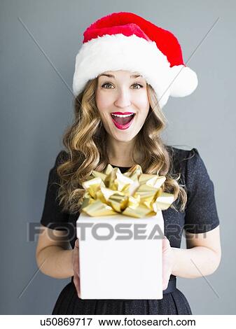 Studio portrait of woman wearing Santa hat holding gift View Large Photo Image Stock Photo - Studio portrait of woman wearing Santa hat holding gift. Fotosearch
