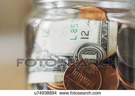 Picture - Studio shot of jar filled with coins and one dollar banknote, close up. Fotosearch